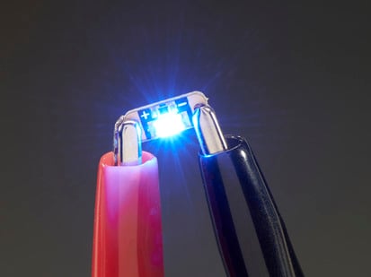 Single LED sequin PCB attached to two alligator clips, glowing blue